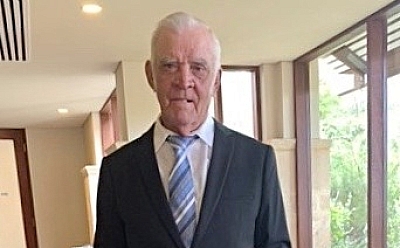 A gentleman dressed in a suit jacket and tie stands holding a cup of tea in his hand