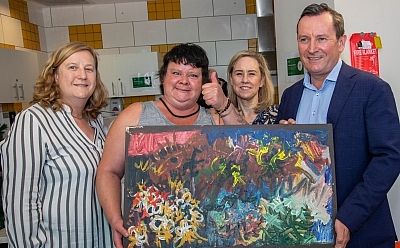 A resident of St Bart's enthusiastically holds up a large colourful artwork with distinctive brush strokes. Premier Mark McGowan holds the other corner of the artwork