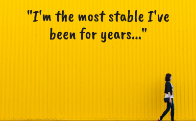 Woman walking along the yellow wall with the following quote written on it: I'm the most stable I've been for years...